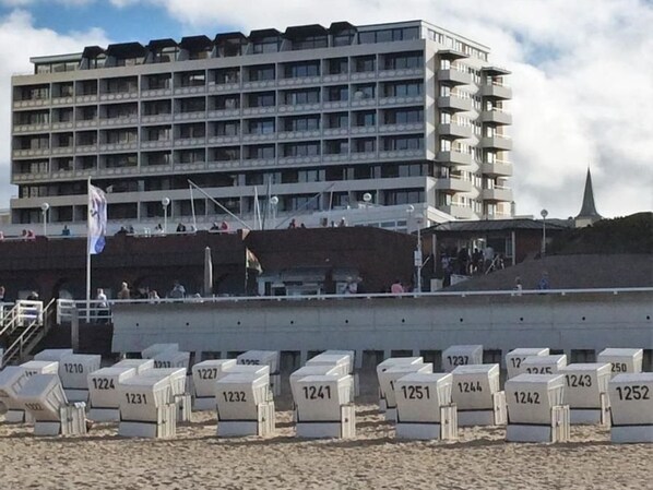 A beach with numbered lounge chairs and a large building in the background. - Haus am Meer14 - App. 138 ob (Sylt)