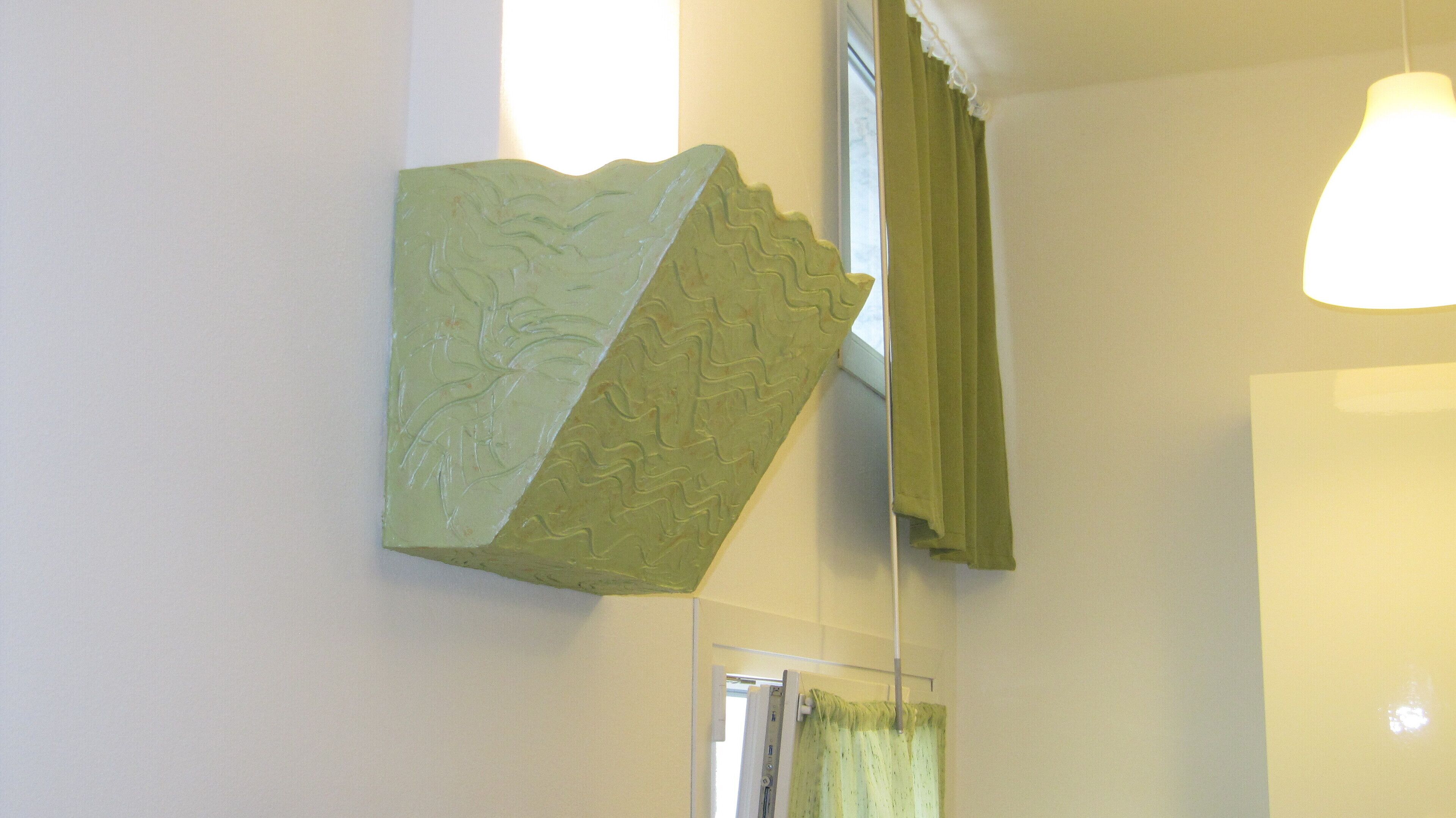 A room with a green textured wall art piece, a window with green curtains, and a hanging light fixture.