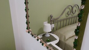 A bedroom with a bed, a bedside table with a lamp, and a mirror with a decorative frame.