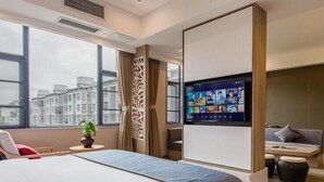 Una moderna camera d'albergo con un letto grande, una televisione montata a parete, un'area salotto con divano e poltrone e vista sulla città da ampie finestre.
