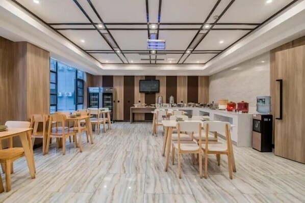 Un comedor moderno con mesas y sillas de madera, suelo de mármol, una encimera de cocina y un televisor montado en la pared.