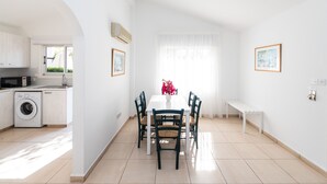 Ein heller, weißer Raum mit Esstisch, Stühlen und einer Bank. Eine Waschmaschine und ein Fenster mit Vorh ängen sind ebenfalls vorhanden.