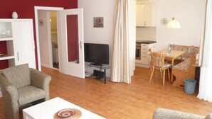A living room with a TV, a dining area with a table and chairs, and a kitchen in the background.
