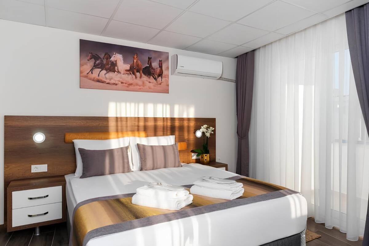 Una habitación de hotel moderna con una cama grande, un cabecero de madera, una mesita de noche con una lámpara y un cuadro de caballos en la pared.
