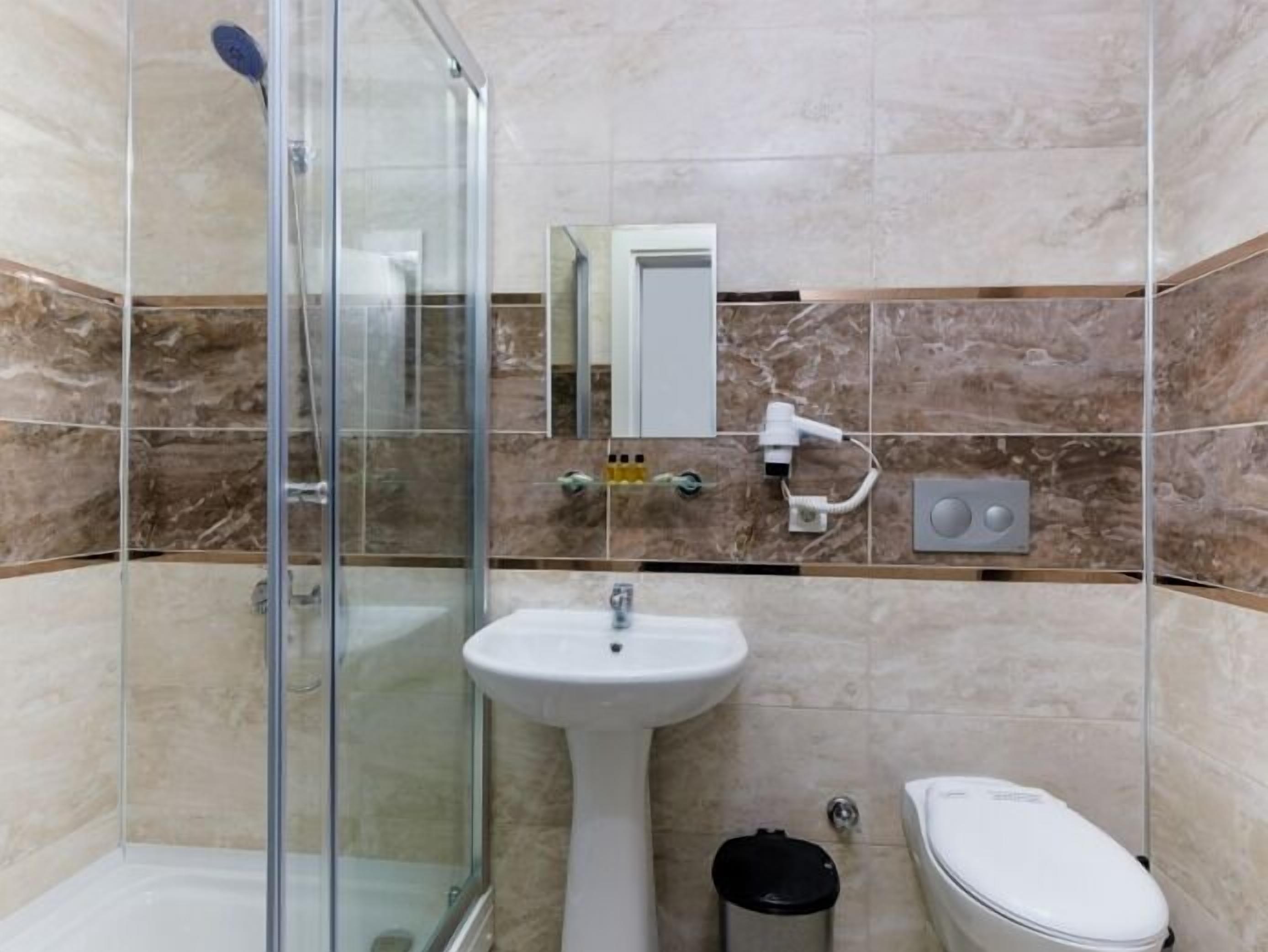 Un baño con cabina de ducha de vidrio, lavabo pedestal, inodoro y espejo.