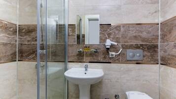 Un baño con cabina de ducha de vidrio, lavabo pedestal, inodoro y espejo.