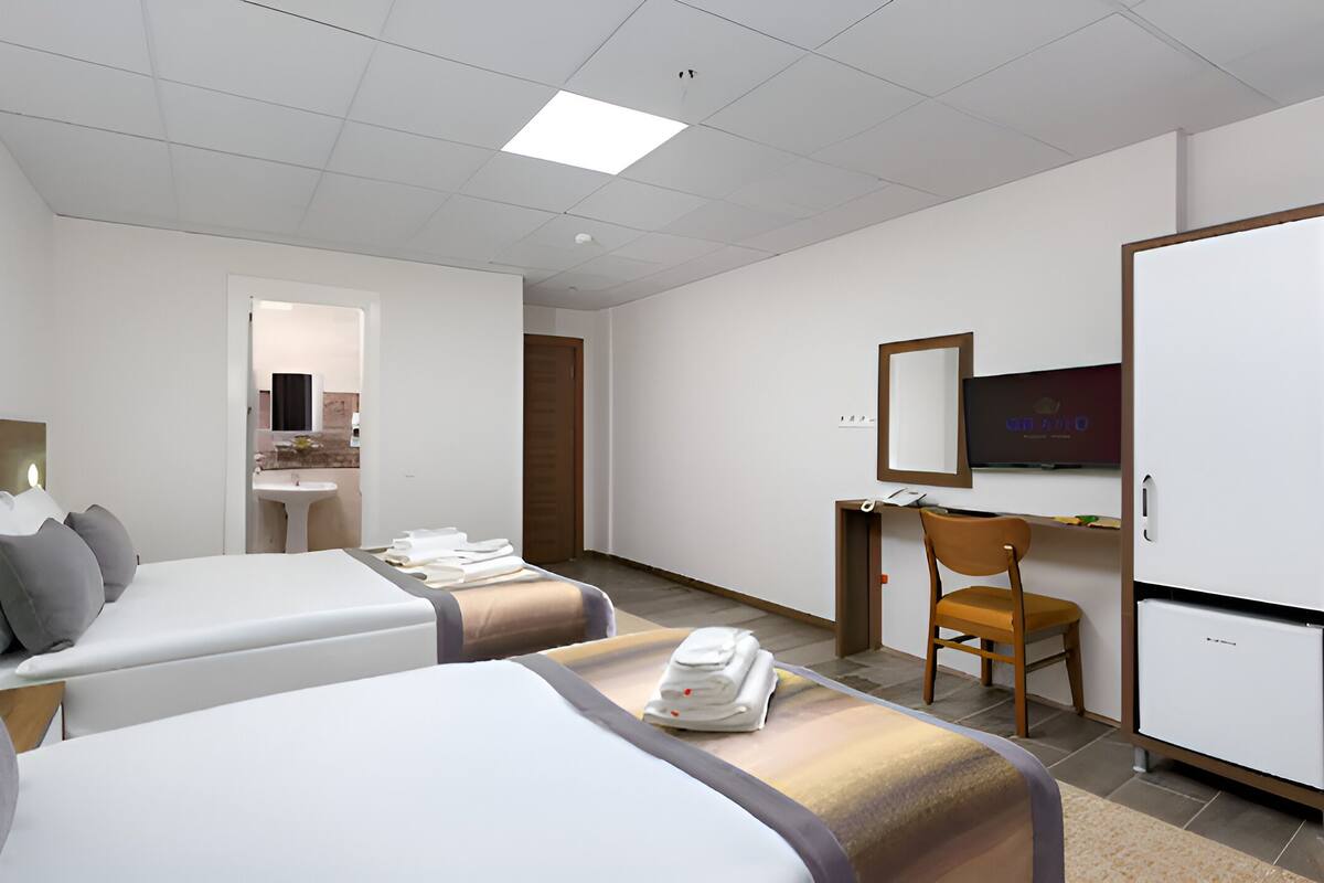 Una habitación de hotel con dos camas, un escritorio, una silla, un televisor y un refrigerador.