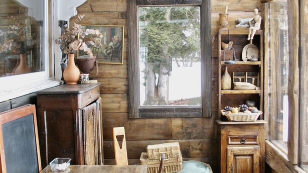 Ein rustikales Blockhaus-Interieur mit einem Holzessttisch, einem Korb aus Weidengeflecht, einem Holzstuhl und einer Kronleuchter aus Geweihen.