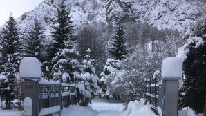 Ein verschneiter Eingangsbereich mit Bergelandschaft im Hintergrund, bewölkter Himmel und einem Weg, der in eine verschneite Landschaft führt.