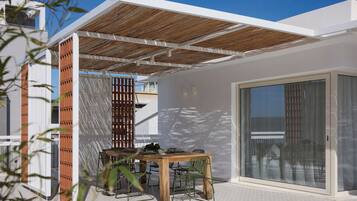 A modern outdoor patio with a wooden table and chairs, a glass door leading to a covered area, and a white exterior wall.