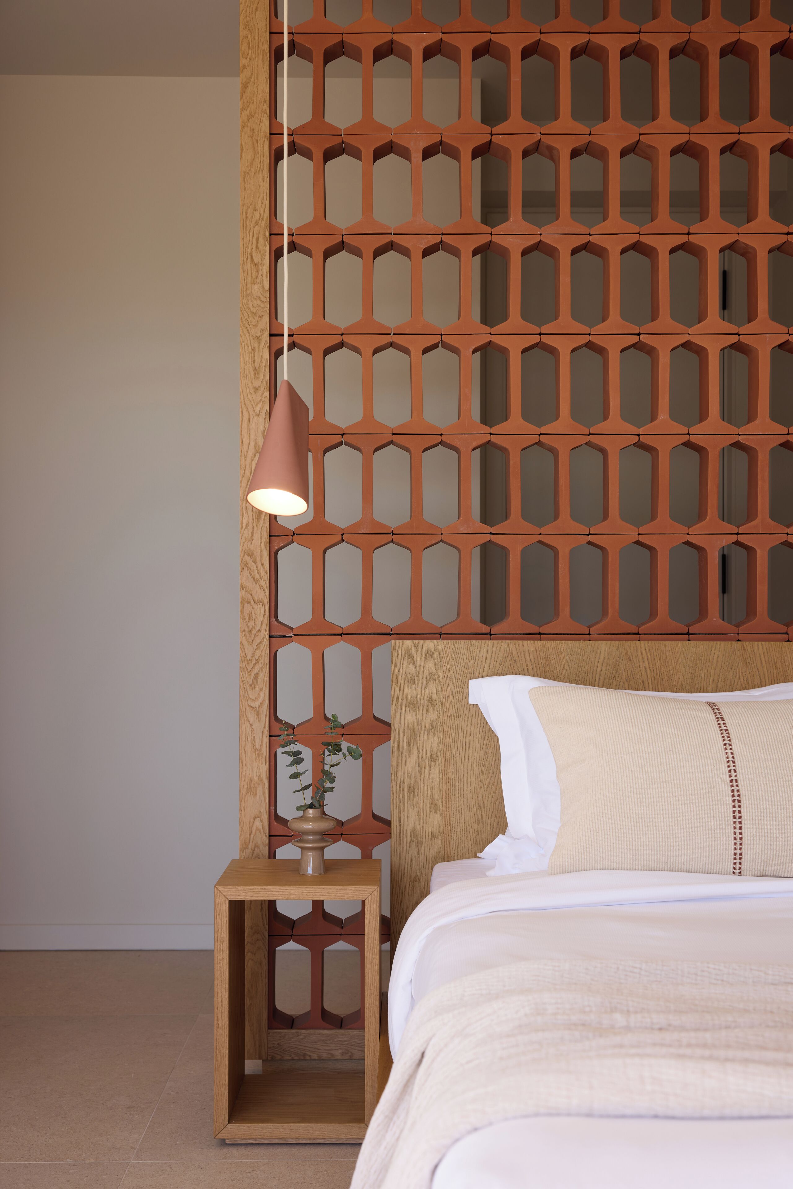 Uma cama bem arrumada com cabeceira de madeira, uma luminária de cabeceira e uma pequena mesa de cabeceira com uma planta.