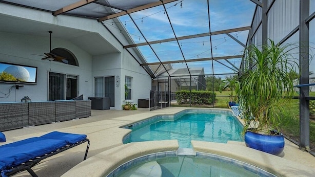 Un espace piscine extérieur moderne, doté d’une structure fermée par des parois de verre, de chaises longues et de plantes en pot.