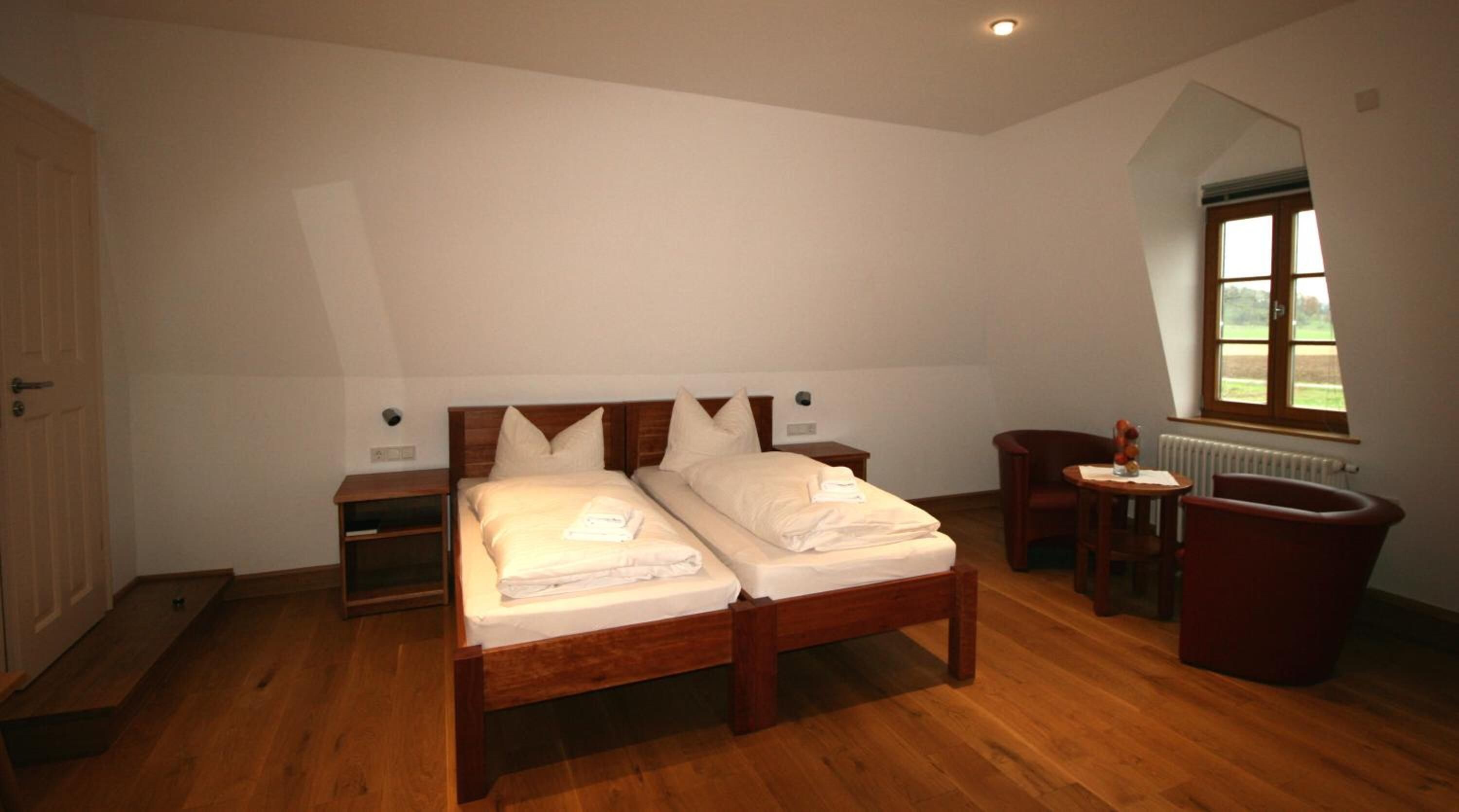 A bedroom with two beds, wooden headboards, a wooden floor, a radiator, a chair, and a window with a view.