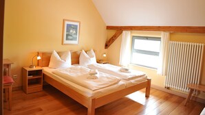 A bedroom with a wooden bed, bedside tables, a nightstand, a window with curtains, and a radiator. - Biohotel Stiftsgut Wilhelmsglücksbrunn (Amt Creuzburg)
