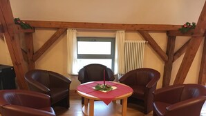 A room with a wooden ceiling, a round table with a red tablecloth, four brown leather chairs, and a window with curtains. - Biohotel Stiftsgut Wilhelmsglücksbrunn (Amt Creuzburg)