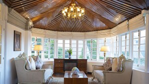 A room with a wooden ceiling, two ornate sofas, a central coffee table, and a fireplace. - The Clovelly Bungalow (Nuwara Eliya)