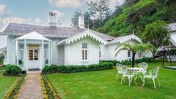 A white colonial-style house with a covered porch, a brick pathway, and a lawn with a table and chairs.
