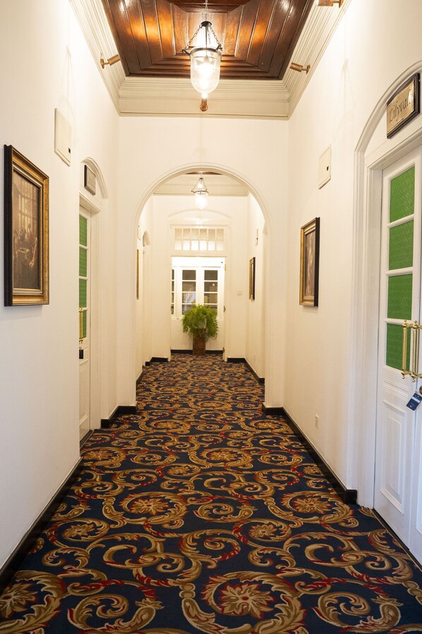 A hallway with a patterned carpet, white walls, and framed artwork. - The Clovelly Bungalow (Nuwara Eliya)
