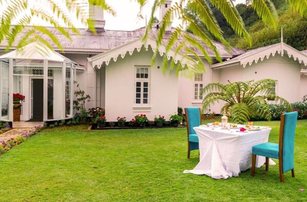 Una casa blanca con un porche cubierto, césped y una mesa lista para comer.