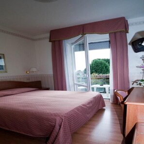 A hotel room with a bed, a desk, a chair, and a window with curtains. - Villa Mulino (Garda)
