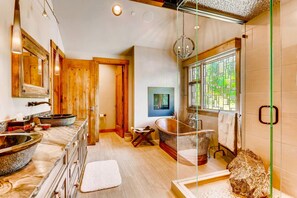 Un baño amplio con una bañera grande, un lavamanos independiente y una zona de ducha con mampara de vidrio.