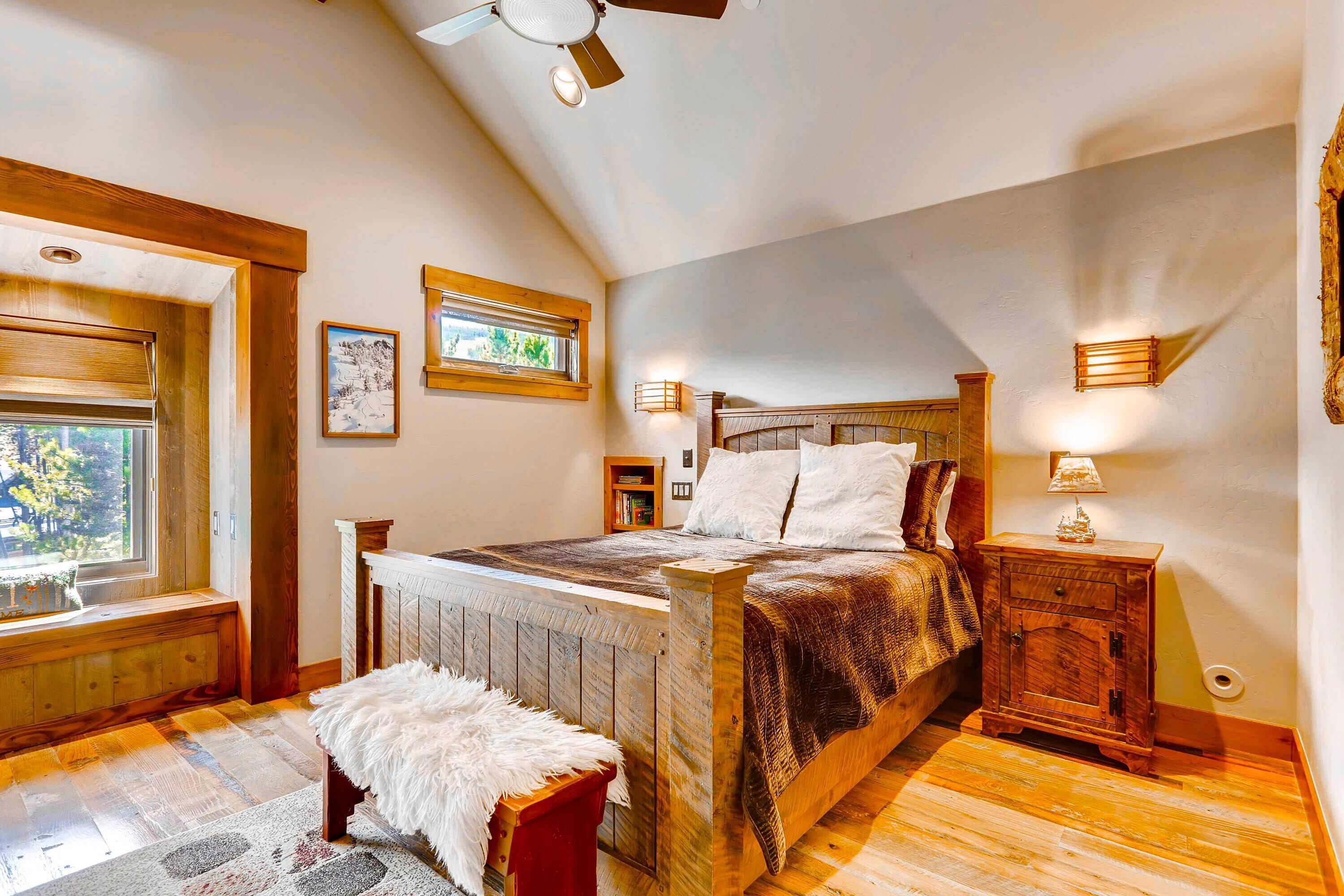 A bedroom with a sloped ceiling, wooden bed frame, and a window with a view of trees.