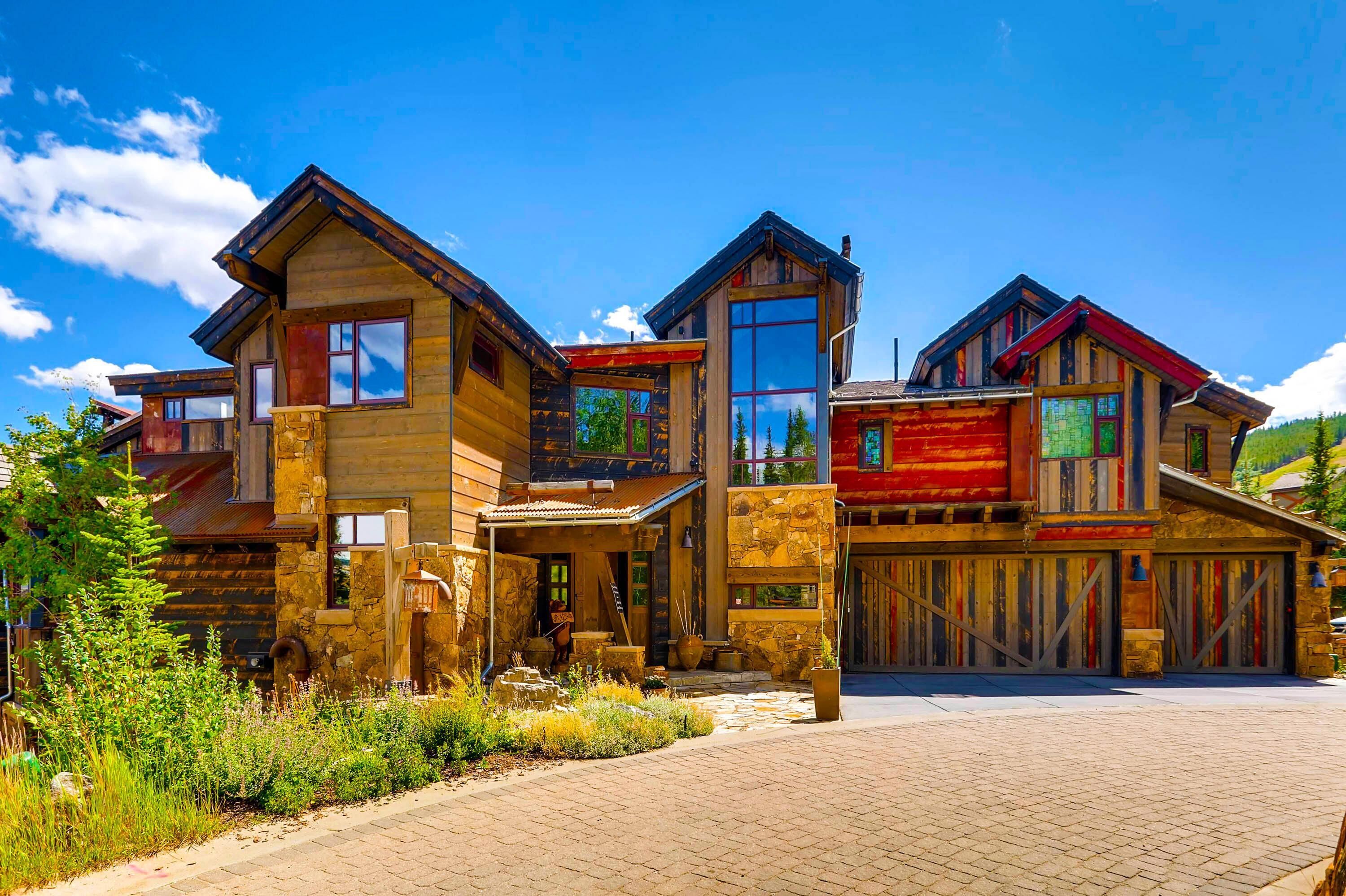 A multi-story log cabin with a stone foundation, large windows, and a covered porch.
