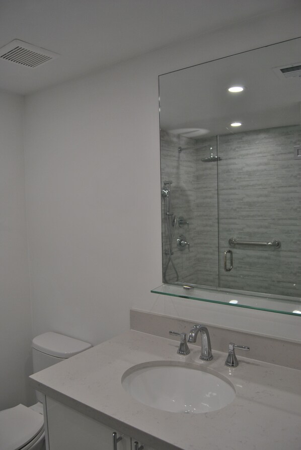 A modern bathroom with a glass shower enclosure, a white sink, and a large mirror. - Newly renovated 3/2 condo on Miami Beach's Alexander Hotel (Miami Beach)