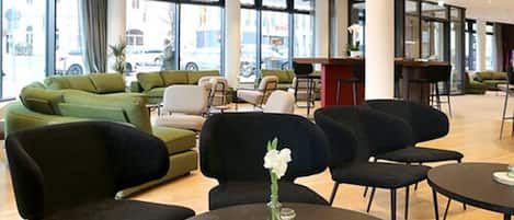 Un moderno vestíbulo de hotel con sofás verdes, sillas negras y mesas redondas.