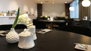 A dining table with a white vase containing a white flower, a white teapot, and a white sugar bowl.