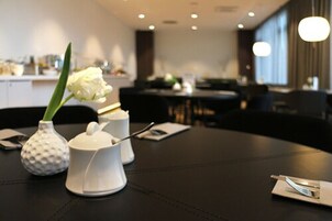 Una mesa de comedor con un jarrón blanco que contiene una flor blanca, una tetera blanca y un azucarero blanco.