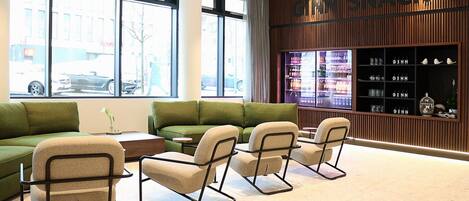 Un intérieur moderne avec un canapé vert, des fauteuils beiges et un présentoir « GINN SNACK ».