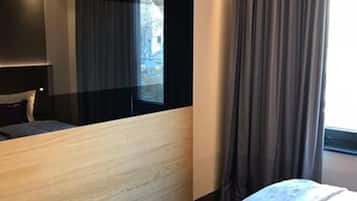Quarto de hotel com cama, mesa de cabeceira, espelho e janela com cortinas.