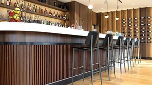 Eine Bar mit einer Holztresen, mehreren Barhocker und einem Weinkühlschrank im Hintergrund.
