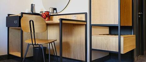 Habitación compacta y moderna con escritorio de madera, una silla, un espejo redondo pequeño y un cesto de basura negro.