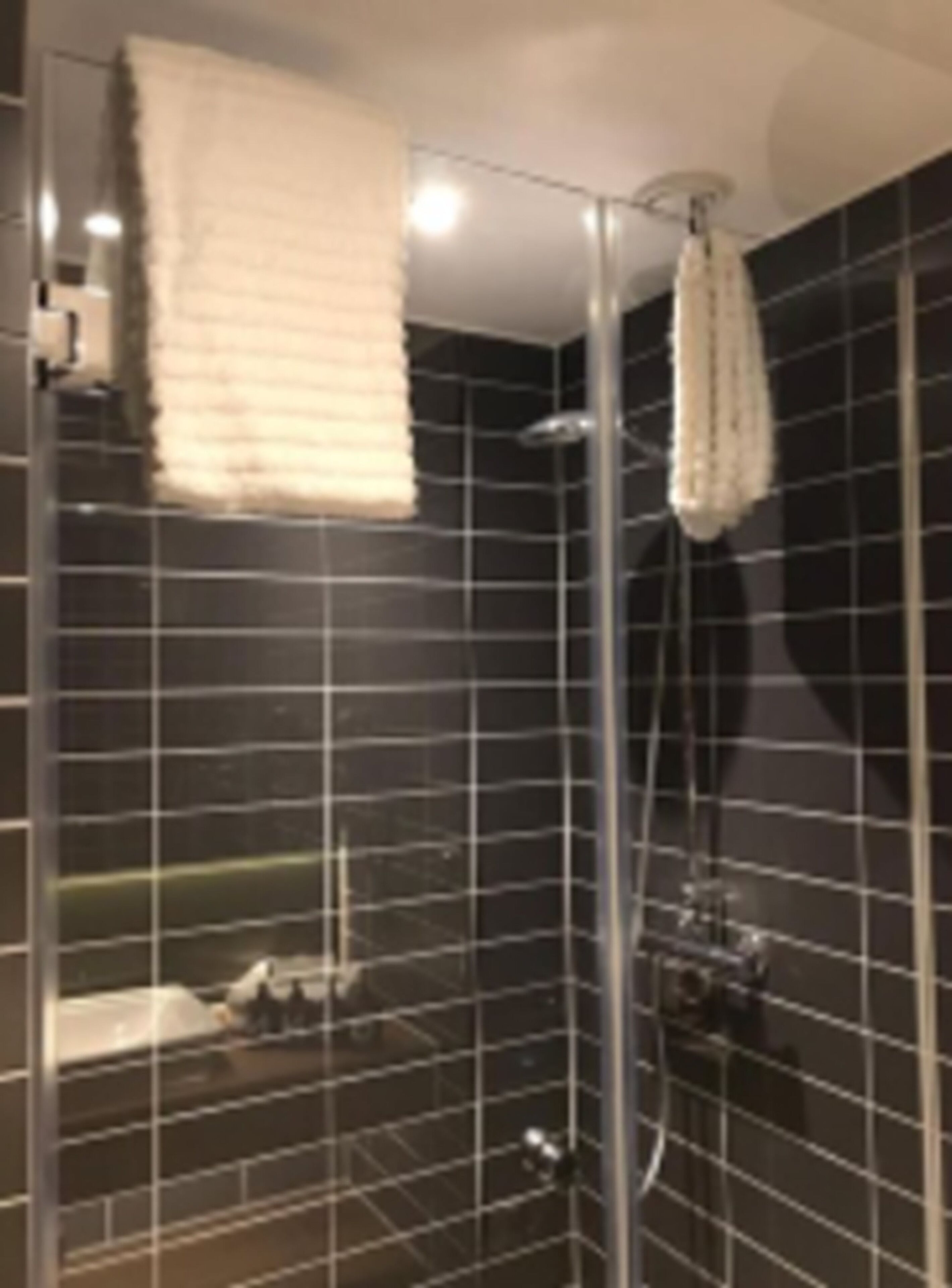 A glass-enclosed shower with a white towel hanging on the wall, a handheld showerhead, and a tiled floor.