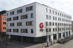 Un edificio moderno con un llamativo logo 'G' en la fachada, varias ventanas y un techo plano.