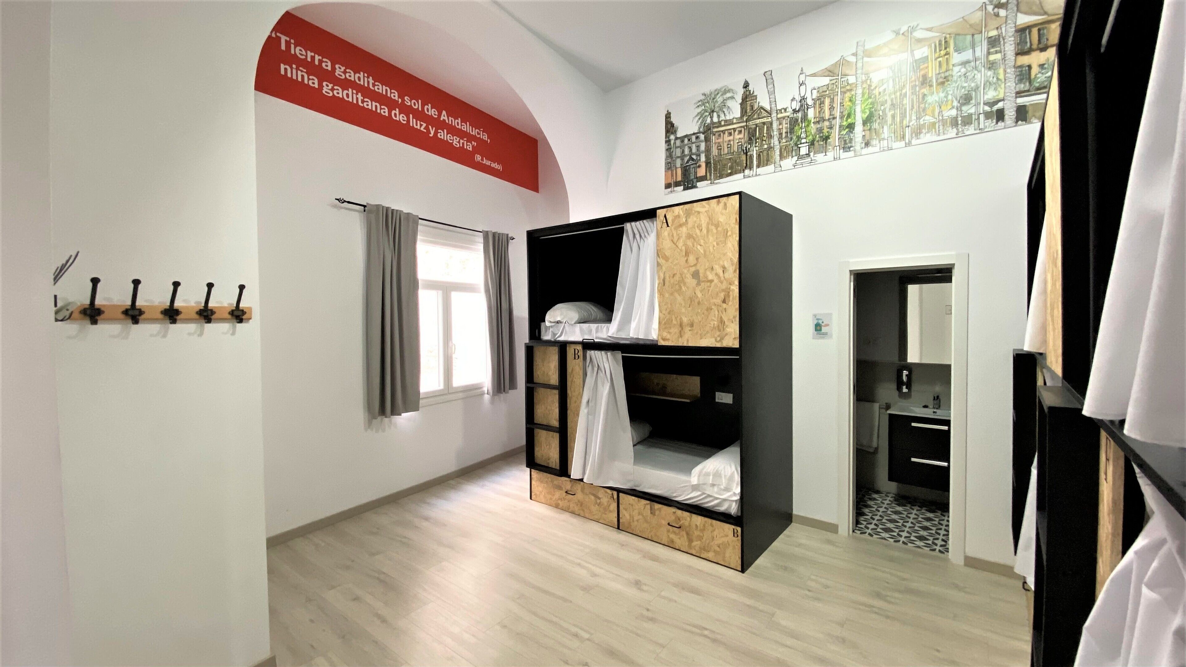 Ein Zimmer mit Etagenbetten, einem Kleiderständer, einem Fenster mit Vorhängen und einer Wand mit einem Zitat.