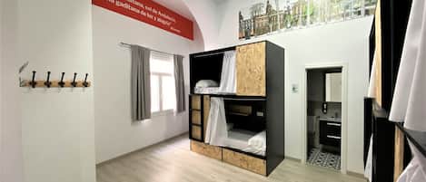 Une chambre avec des lits superposés, un porte-manteau, une fenêtre avec des rideaux et un mur orné d’une citation.