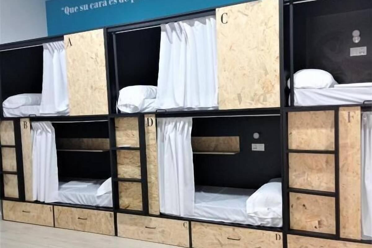 A row of bunk beds with wooden panels and white bedding, in a room with a blue wall and a motivational quote.