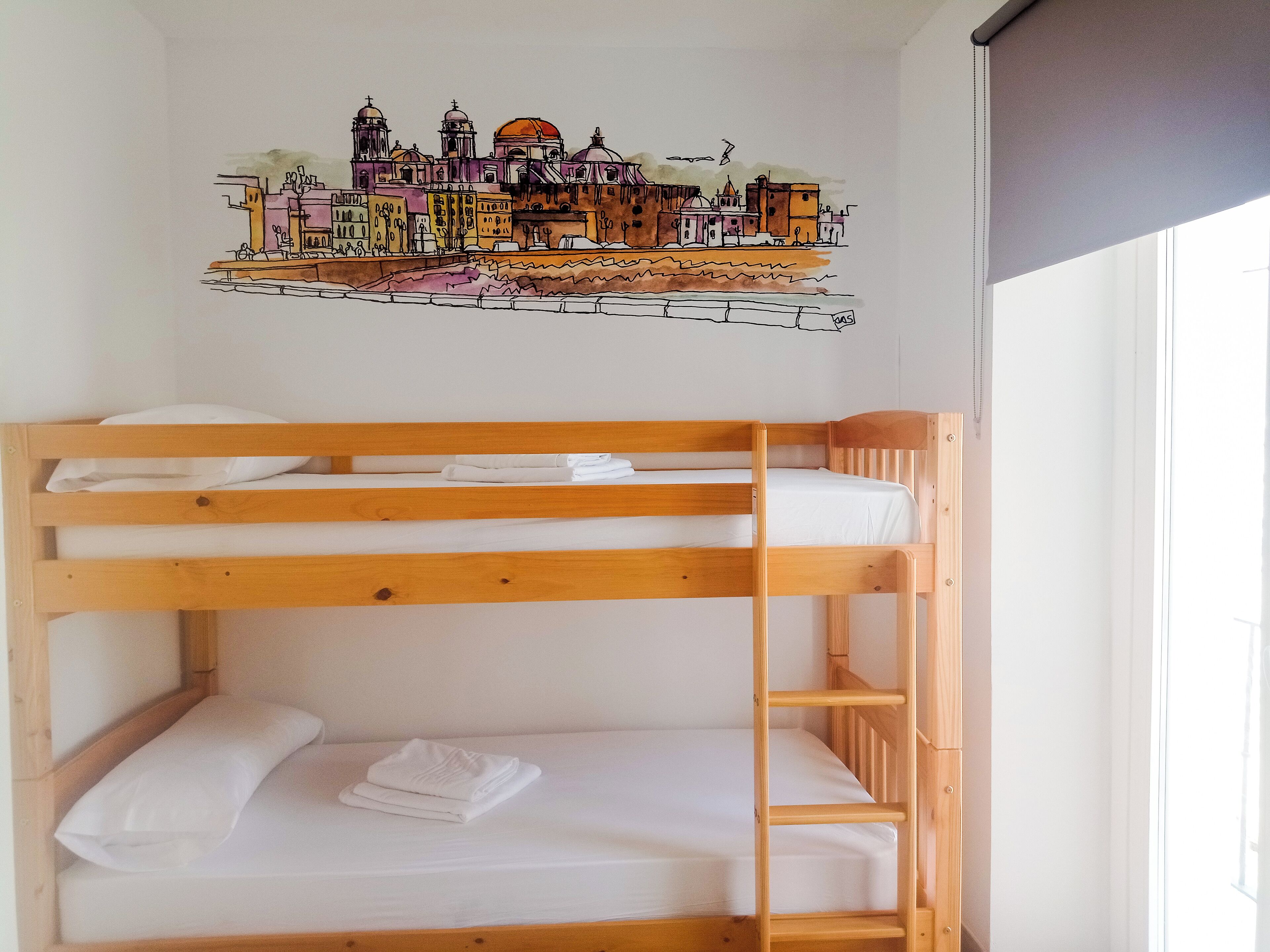 A bunk bed with white bedding and a cityscape mural on the wall.