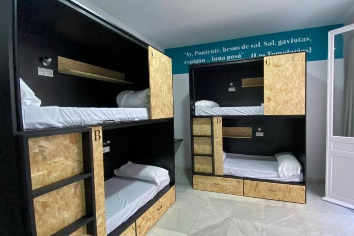 A dormitory room with bunk beds labeled A, B, C, and D. There is a window on the left and a door on the right.