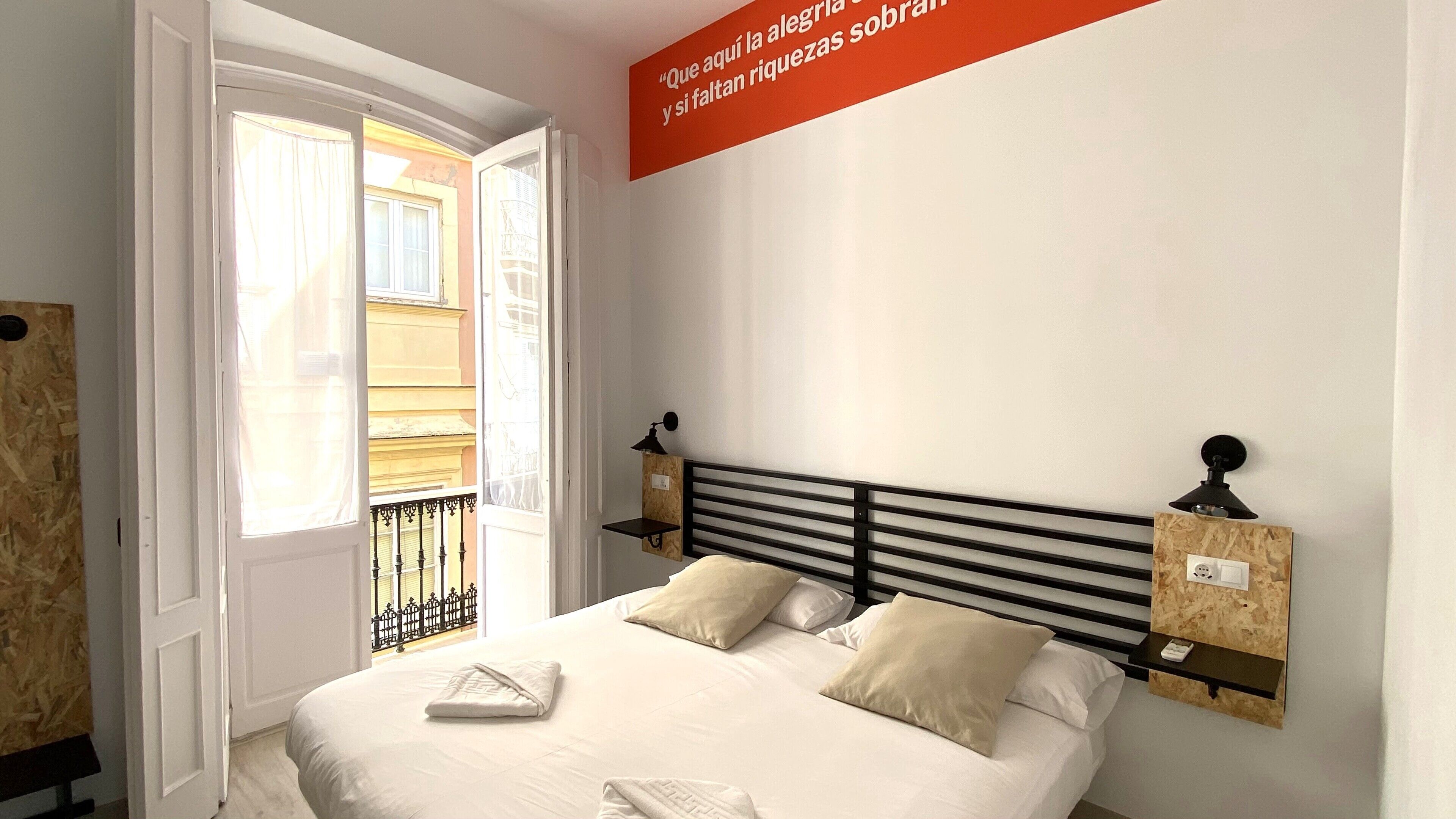 A bedroom with a bed, two bedside tables, a window, and a wall-mounted sign.