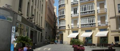 A pedestrian street with benches, a café, and a building with multiple balconies.