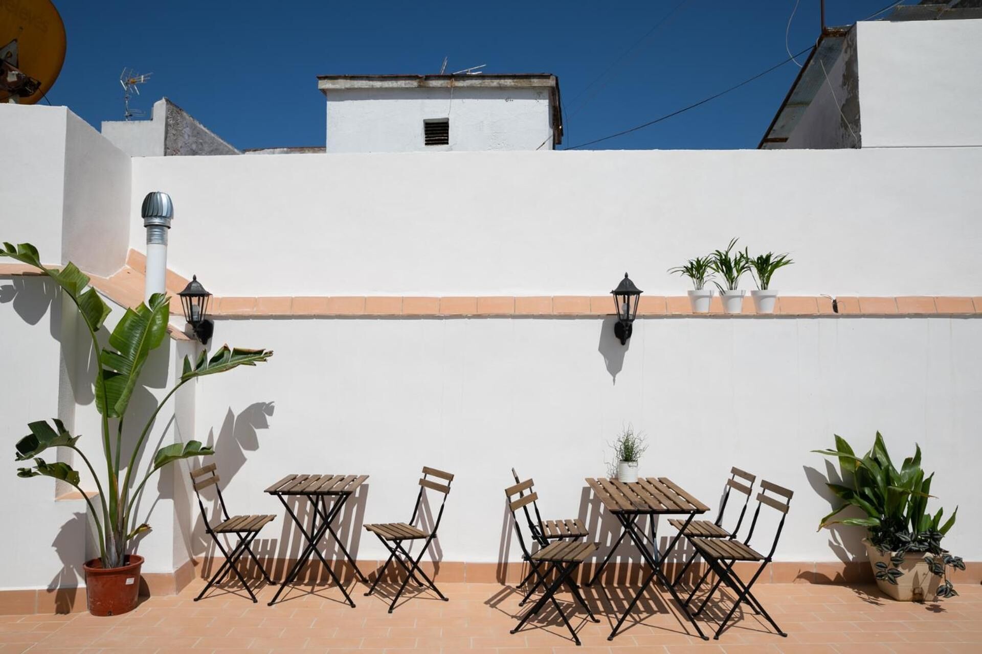 An outdoor patio with a white wall, a tiled floor, and a table with chairs.