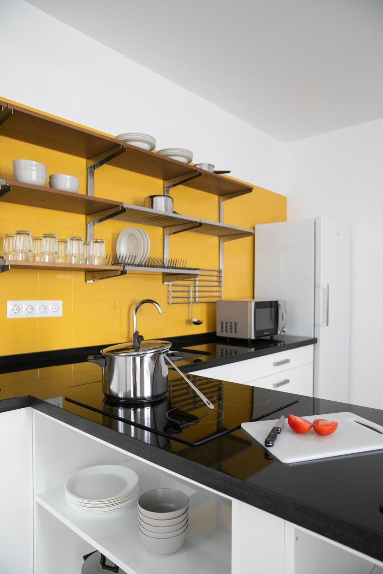 Une cuisine moderne avec un plan de travail noir, des appareils en acier inoxydable et un pare-feu jaune.