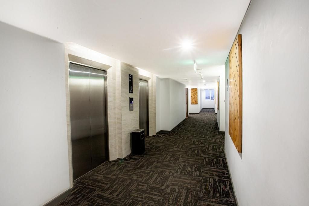 A hallway with two elevators, a trash bin, and a wooden panel on the wall.
