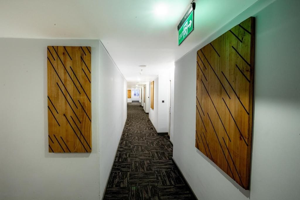 A hallway with a carpeted floor, wooden panel walls, and a green exit sign.