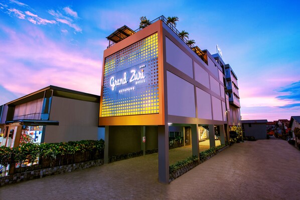 Un hotel con un letrero iluminado grande, un espacio exterior cubierto y una entrada pavimentada.
