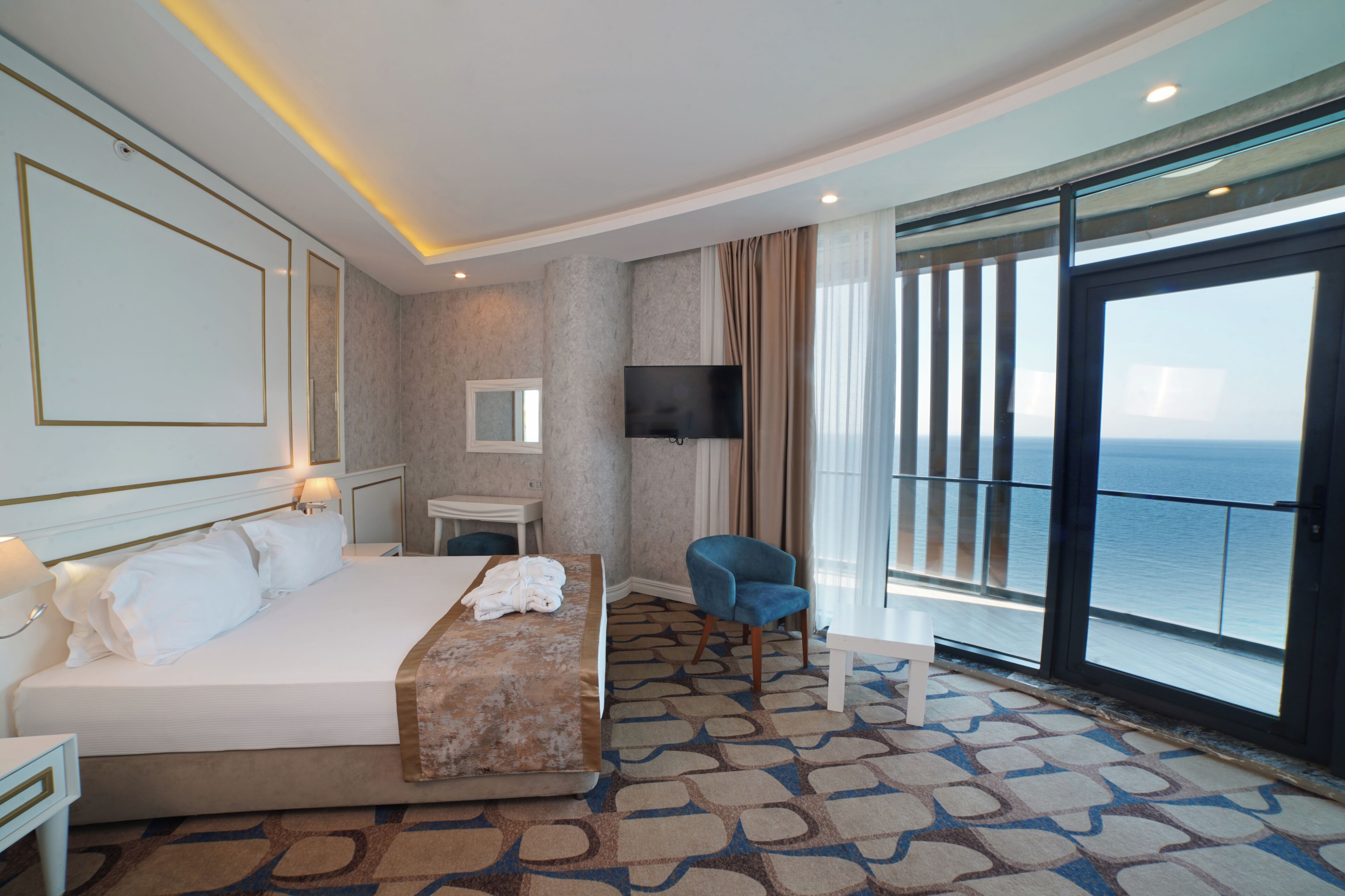 A hotel room with a bed, a desk, a chair, a TV, and a balcony with a view.